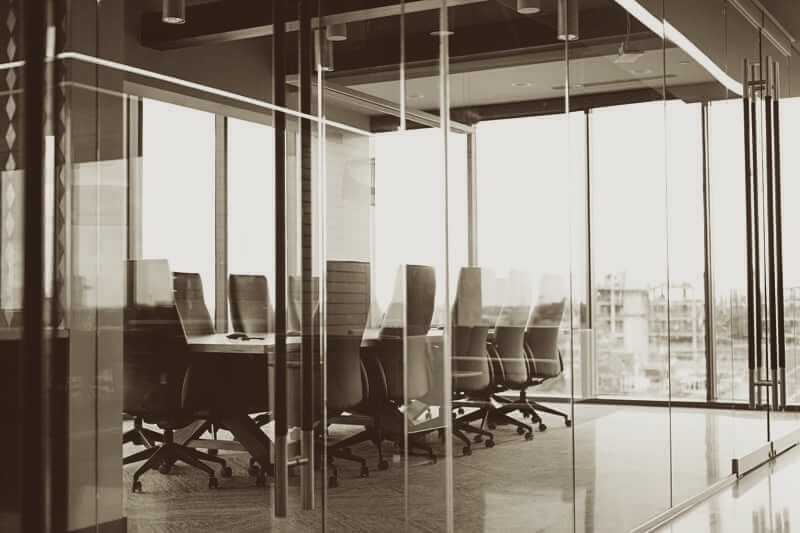 A group of three people in uniforms cleaning an indoor space filled with plants. One person is vacuuming with a wet/dry vacuum, while the others are tending to plants. The setting features a modern, well-lit environment with stairs in the background.